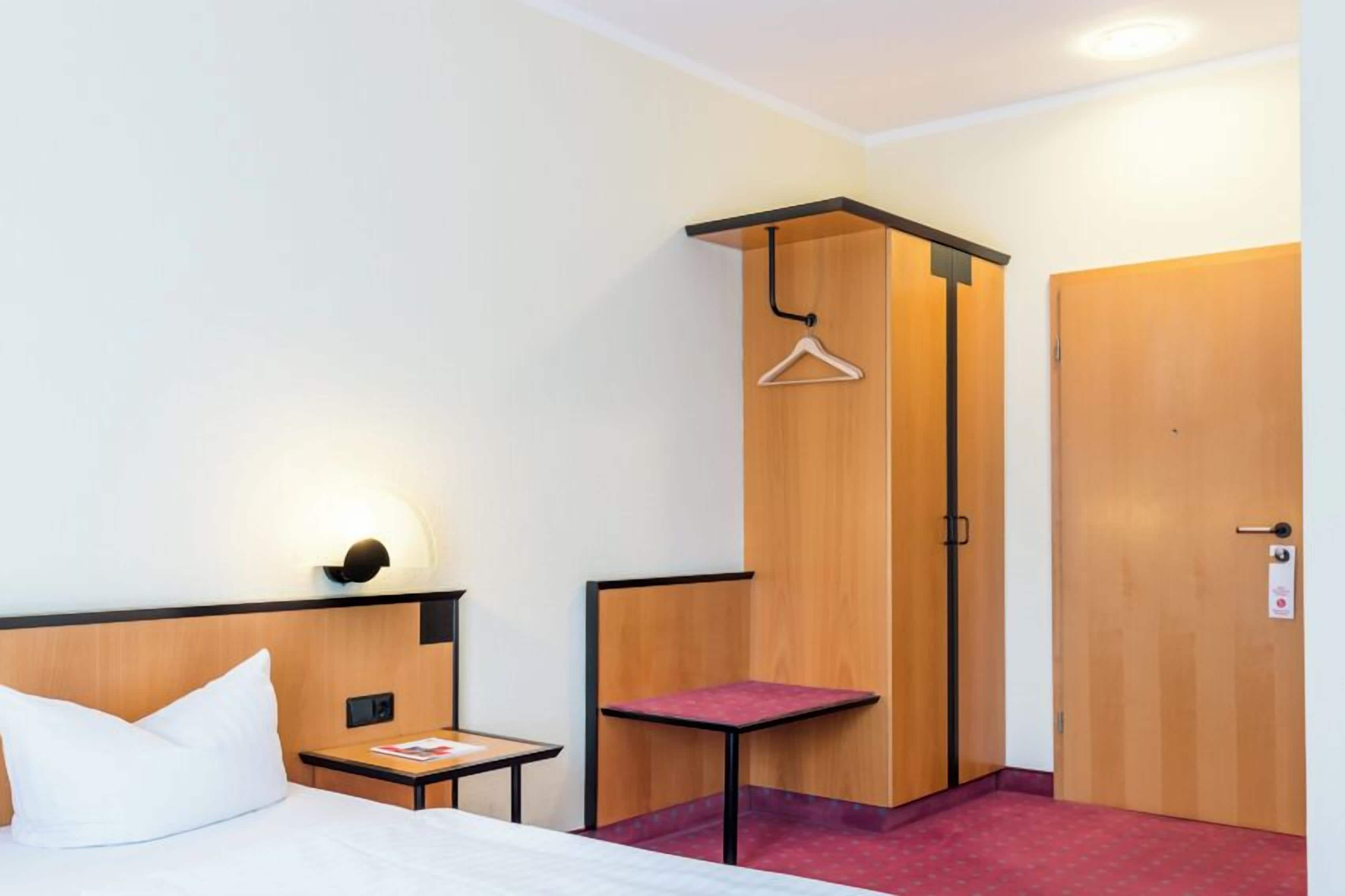 Une chambre d’hôtel avec un lit, une petite table, un porte-manteau et une porte.