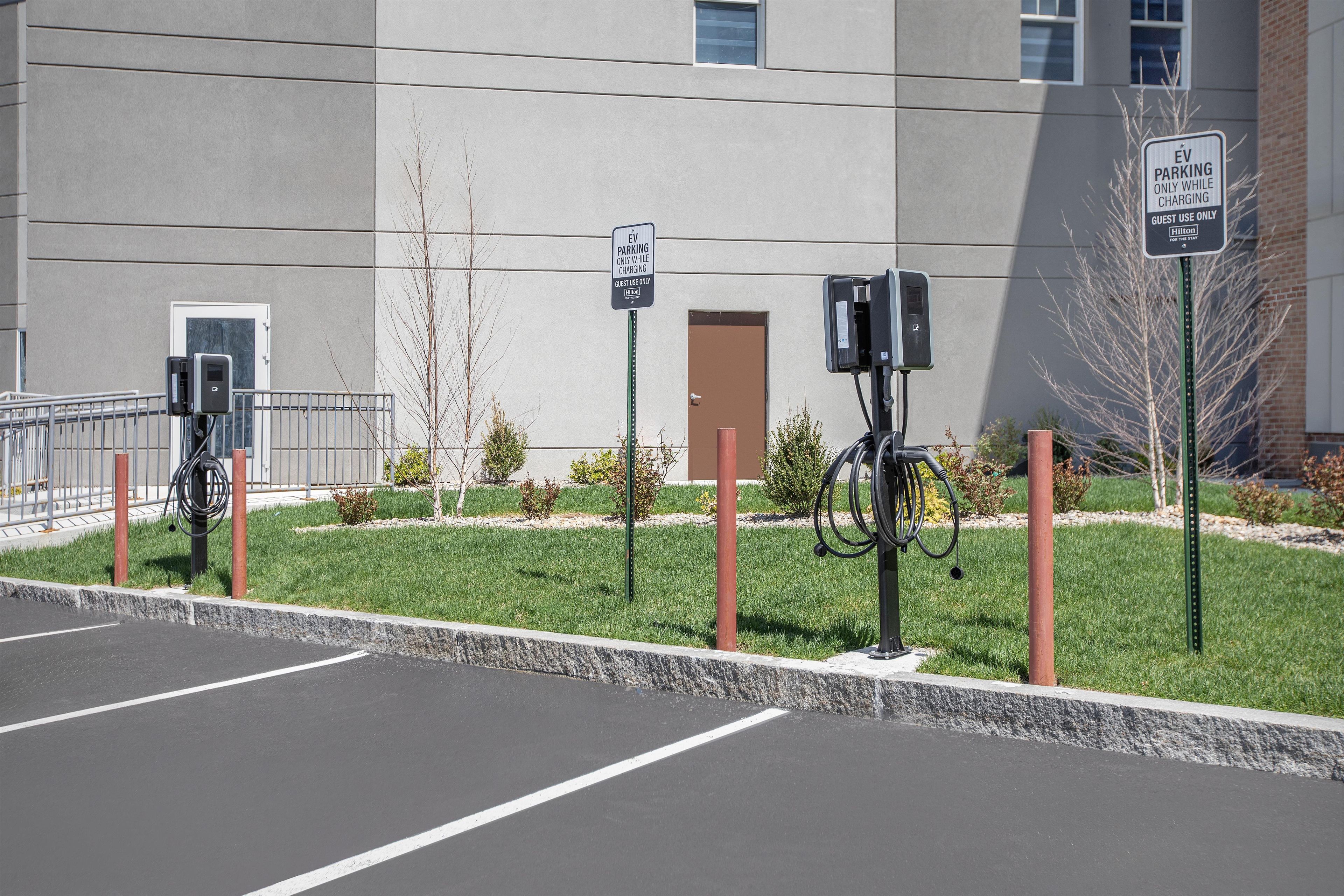 A parking area with electric vehicle charging stations, a sign indicating guest-only use, and a building with a flat facade.