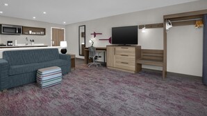 A modern hotel room with a kitchenette, a flat-screen TV, a sofa, a desk, and a chair. - Home2 Suites by Hilton Chelmsford Lowell (Chelmsford)