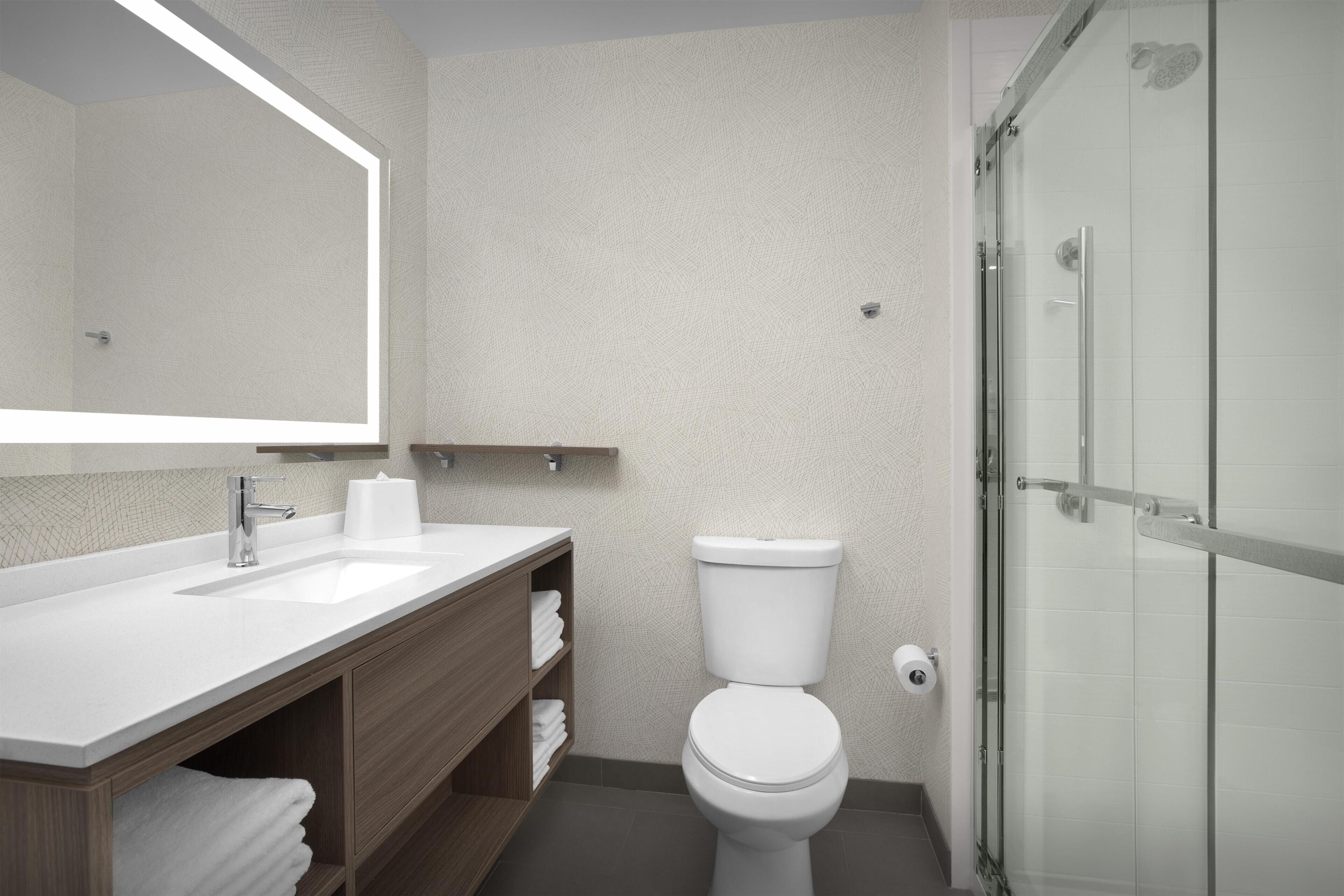 Un baño con lavamanos blanco, inodoro, cabina de ducha de vidrio y espejo sobre el lavamanos.