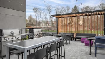 An outdoor patio with a grill, seating, and a view of a park.