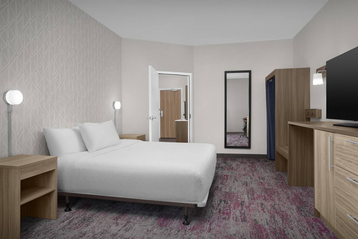 A hotel room with a bed, bedside tables, a mirror, a wardrobe, and a television.