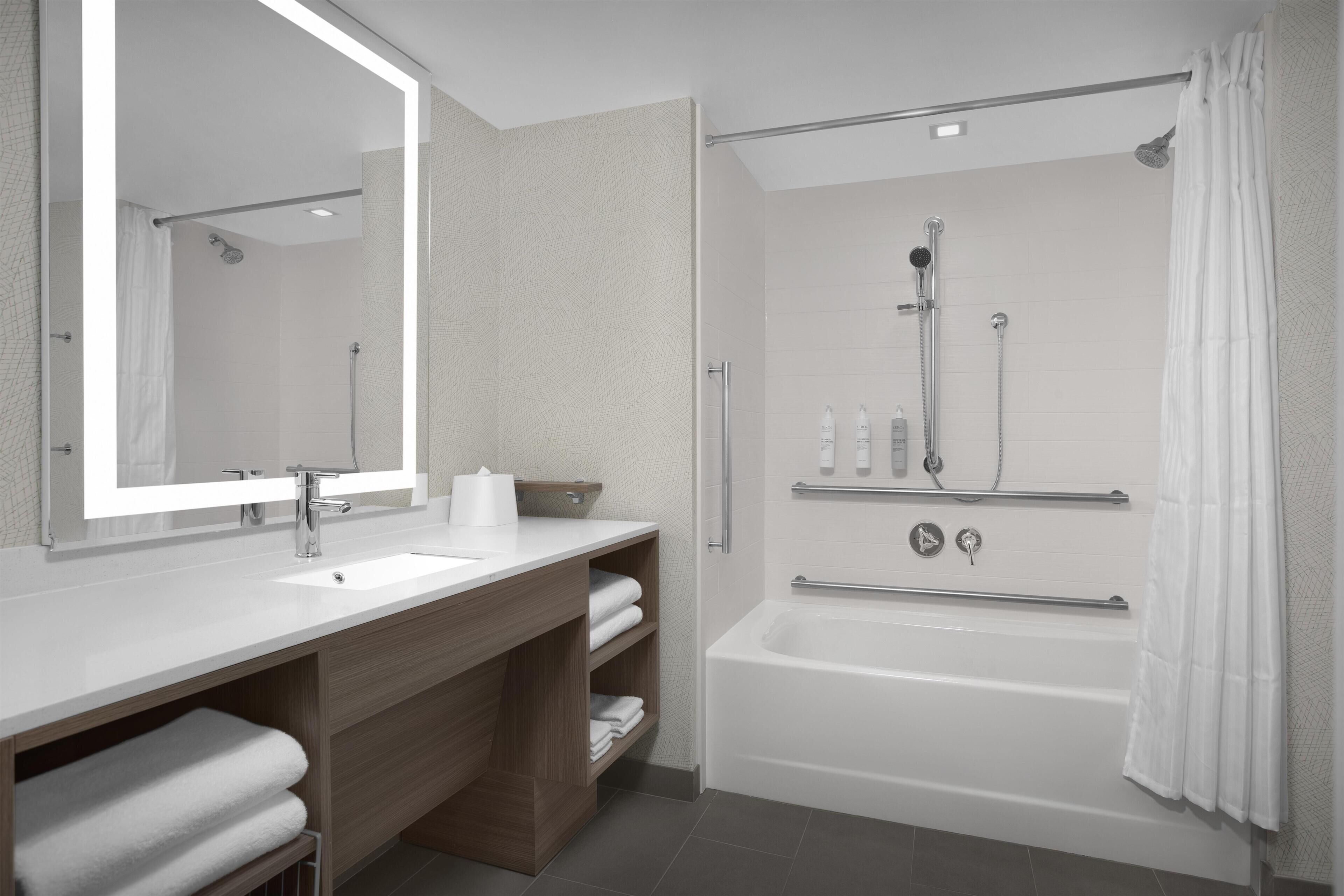 Un baño moderno con bañera, un espejo grande y un tocador con lavabo y toallero.