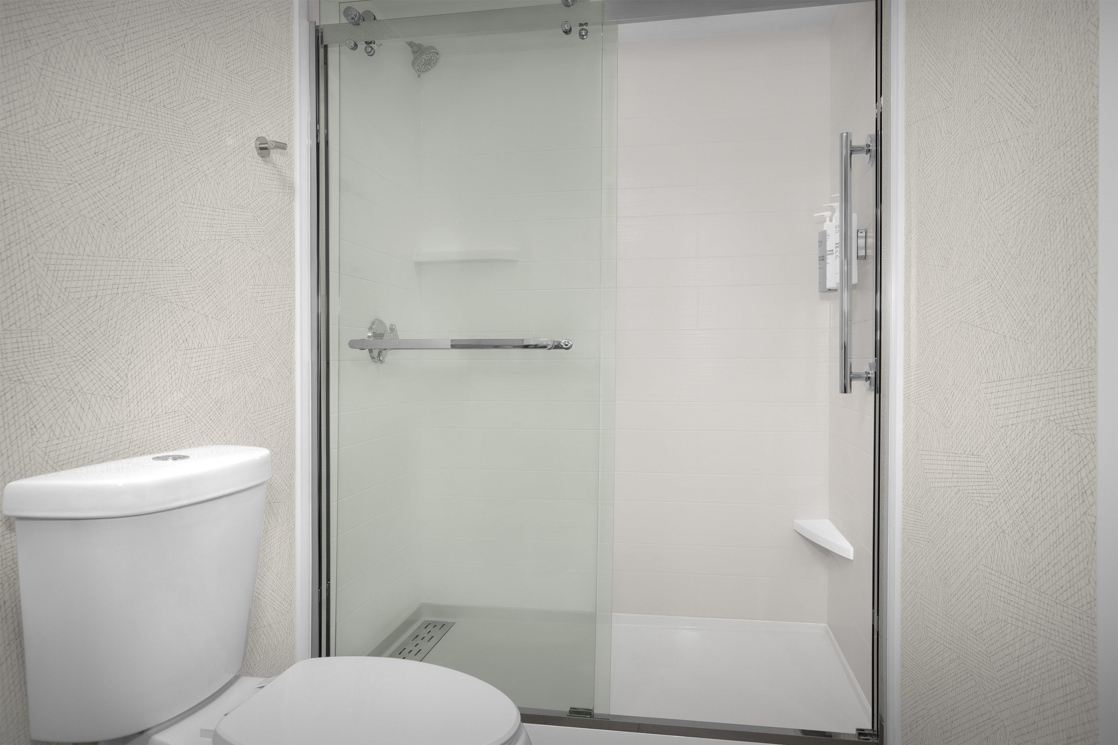 A bathroom with a toilet, a glass-enclosed shower, and a white tiled wall.