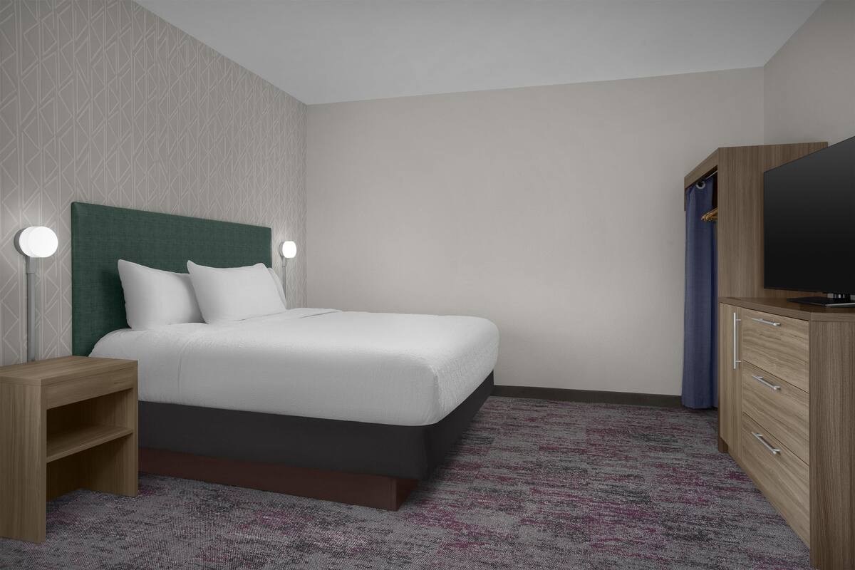 A hotel room with a bed, bedside tables, a TV, and a wardrobe.