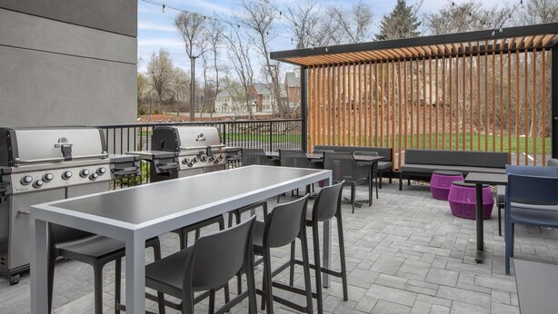 An outdoor patio with a grill, seating, and a view of a park. - Home2 Suites by Hilton Chelmsford Lowell (Chelmsford)