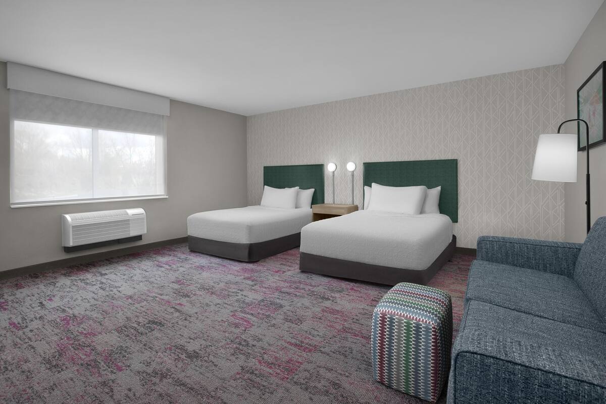A hotel room with two beds, a sofa, a patterned carpet, and a window with blinds.