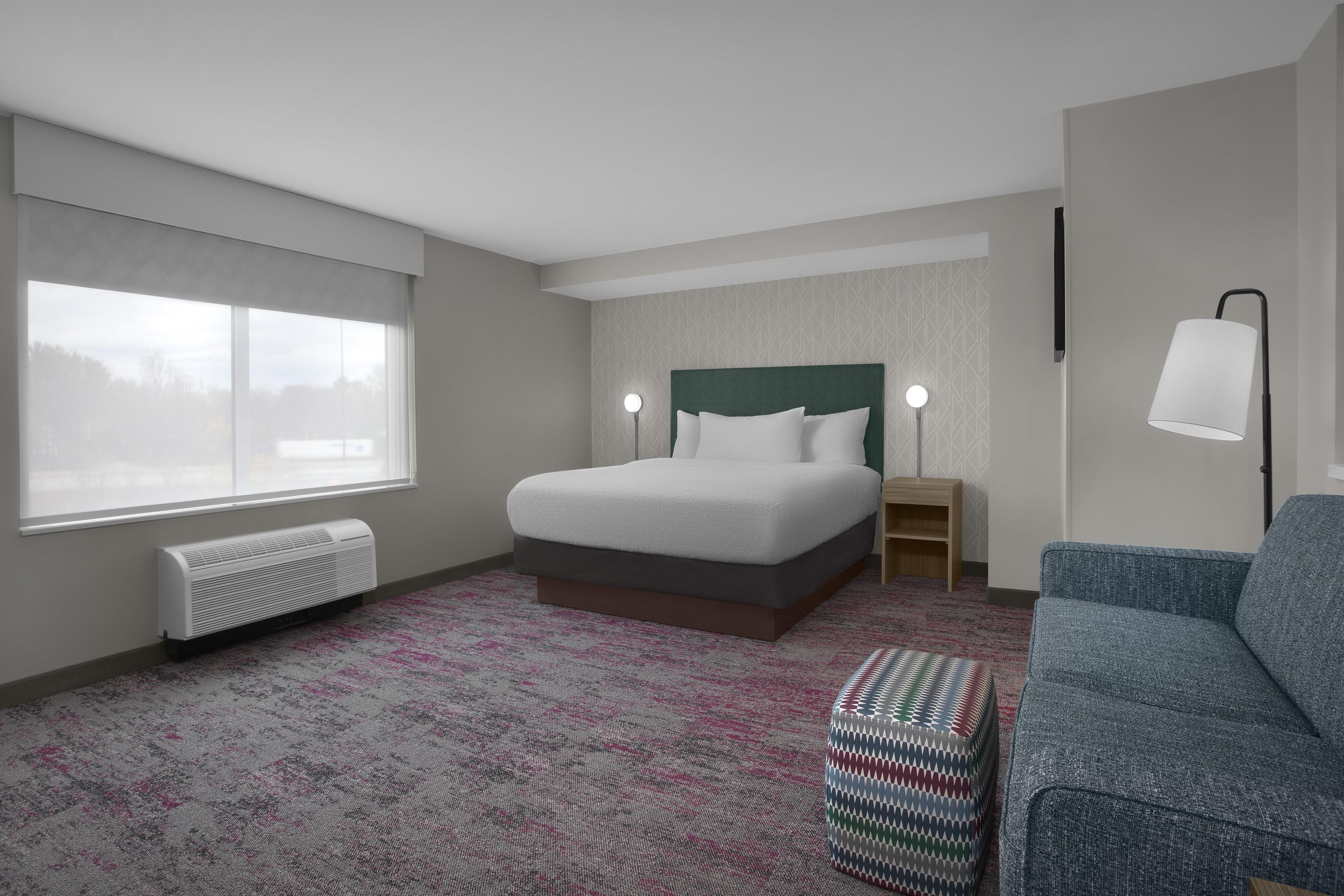 Una habitación de hotel con cama, ventana, calefactor, lámpara y sofá.