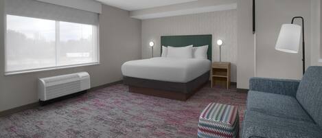 A hotel room with a bed, a window, a heater, a lamp, and a couch.