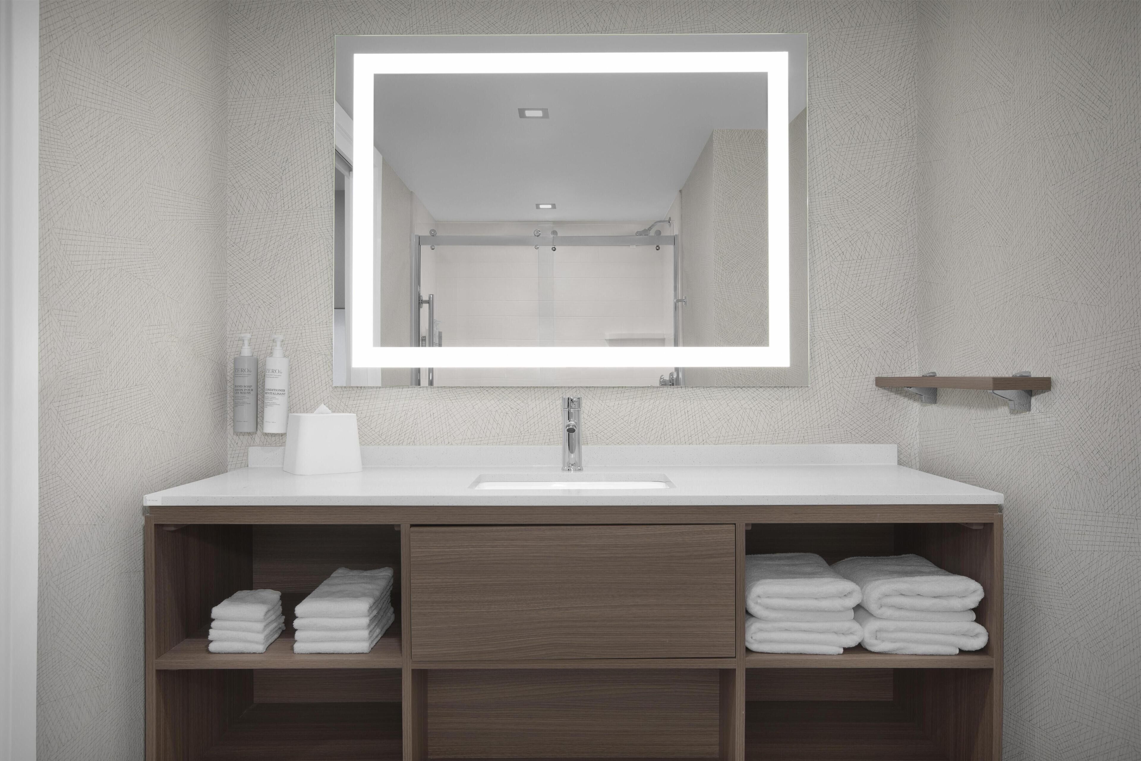 Une salle de bain avec un lavabo blanc, un miroir et des étagères en bois où sont pliées des serviettes.