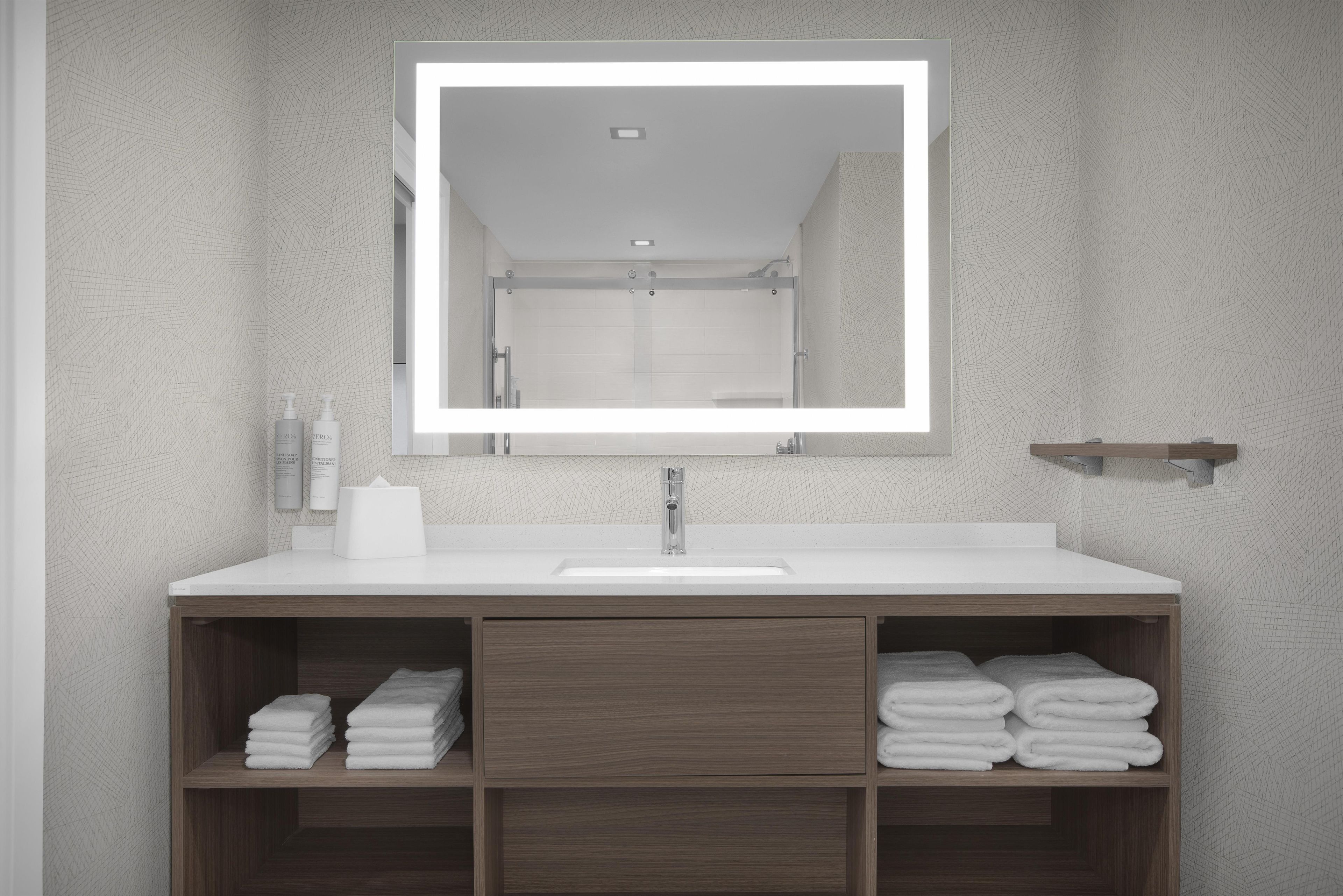 Un baño con lavamanos blanco, un espejo y estantes de madera con toallas dobladas.
