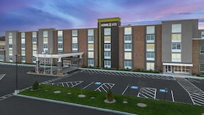 A multi-story hotel with a central entrance, parking lot, and a clear sky. - Home2 Suites by Hilton Chelmsford Lowell (Chelmsford)