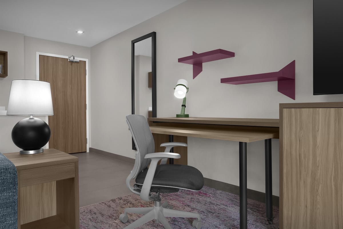 A modern office space with a desk, chair, lamp, mirror, and decorative wall elements.