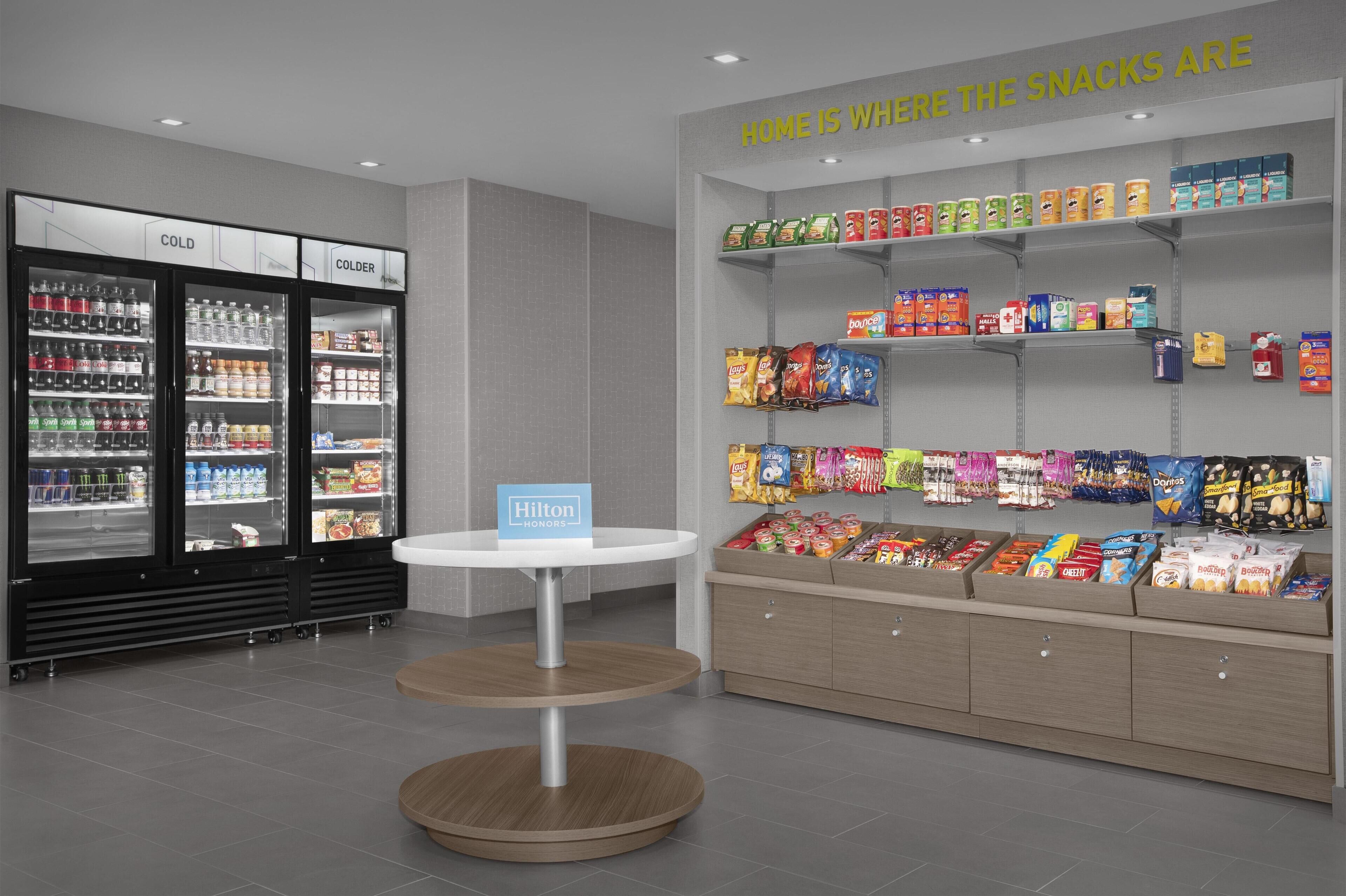 A hotel snack area with a refrigerated section, a display of snacks, and a Hilton Honors sign.