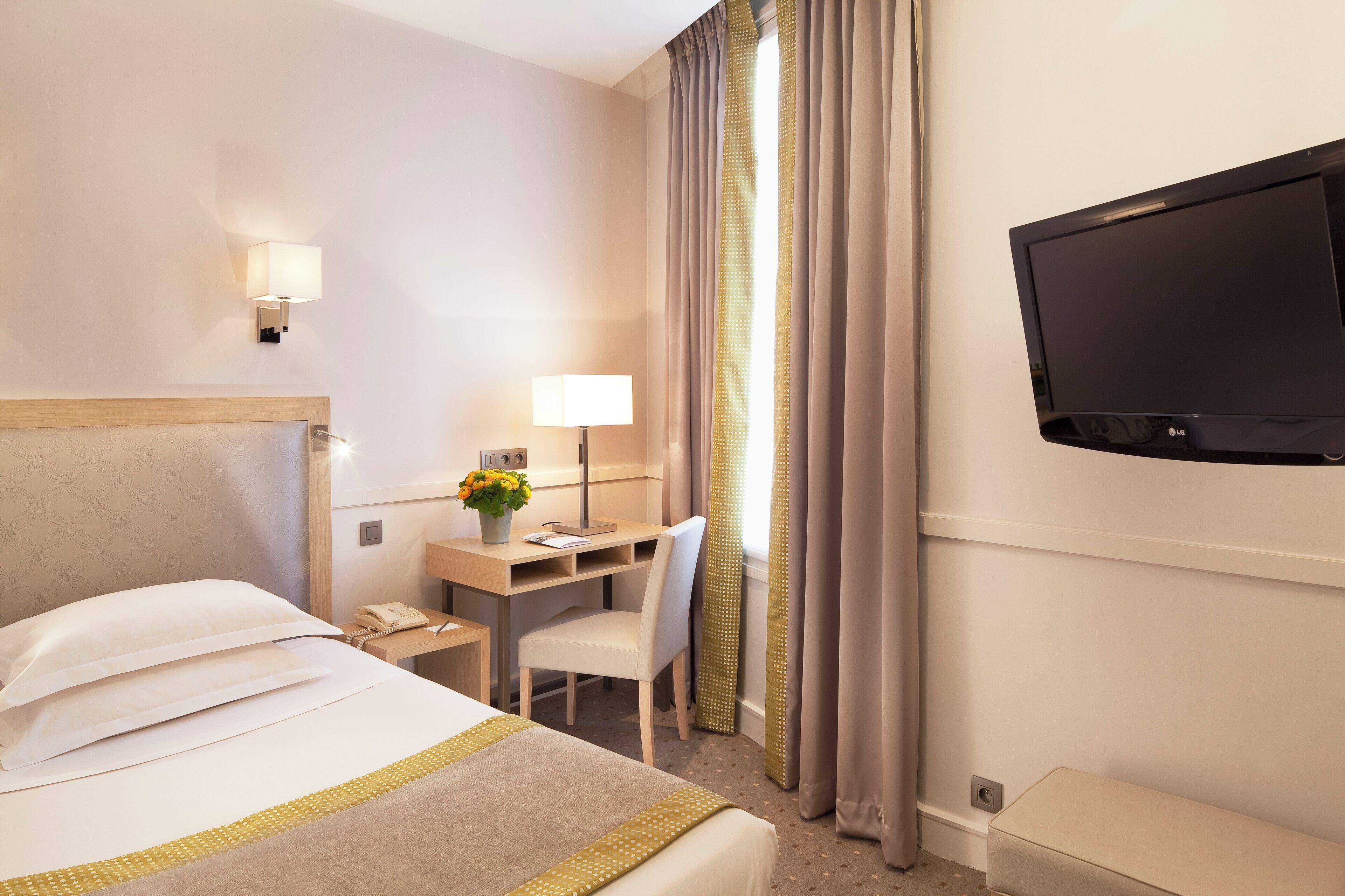 Une chambre d’hôtel équipée d’un lit, d’un bureau, d’une chaise, d’une lampe, d’une télévision et de rideaux.