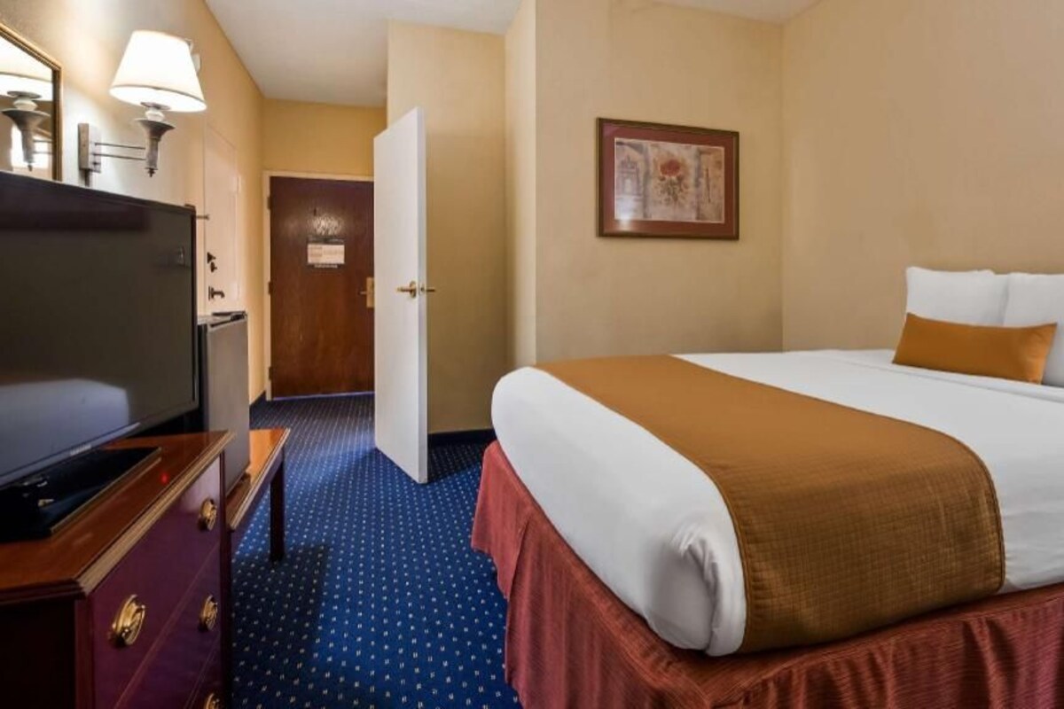 A hotel room with a bed, a television, a desk, and a door.