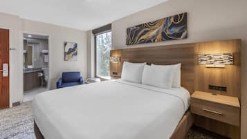A hotel room with a large bed, a wooden headboard, a nightstand, a wall-mounted lamp, and a painting above the bed.