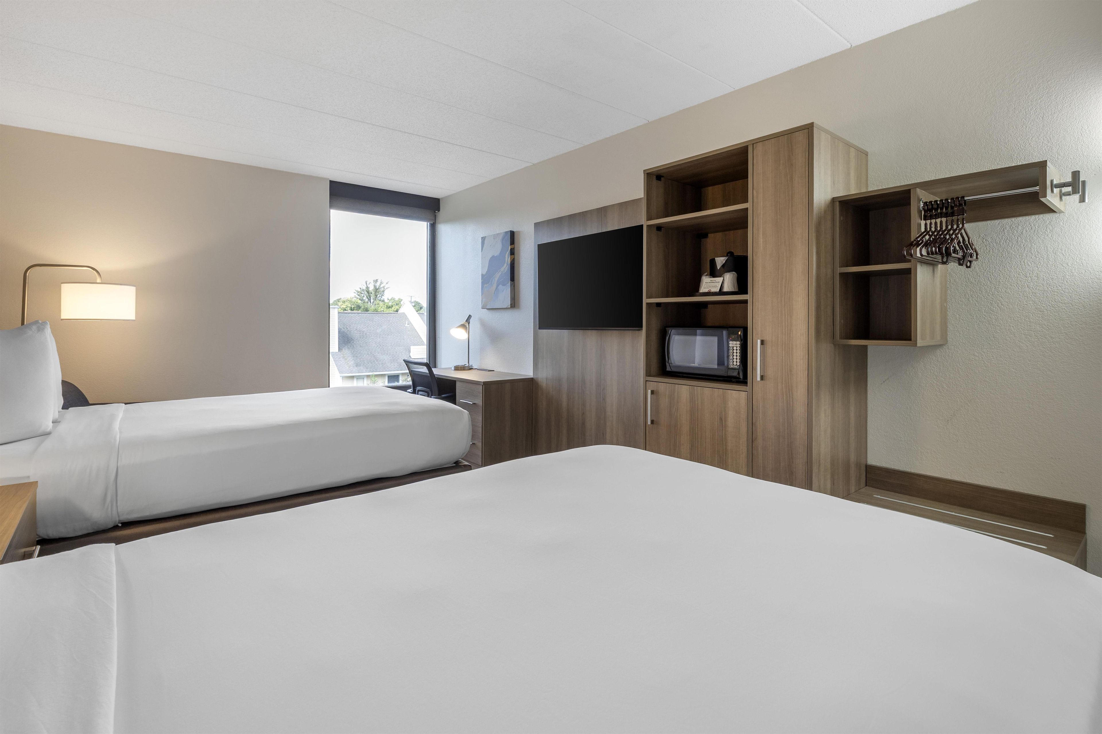 A hotel room with two beds, a desk, a flat-screen TV, a microwave, and a wardrobe.