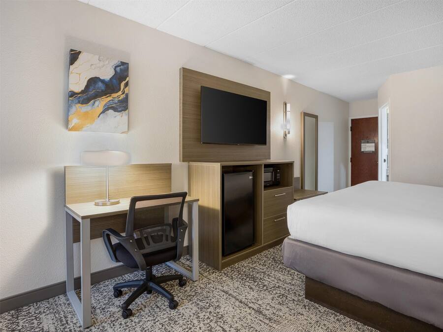 A hotel room with a bed, desk, chair, TV, and a microwave.