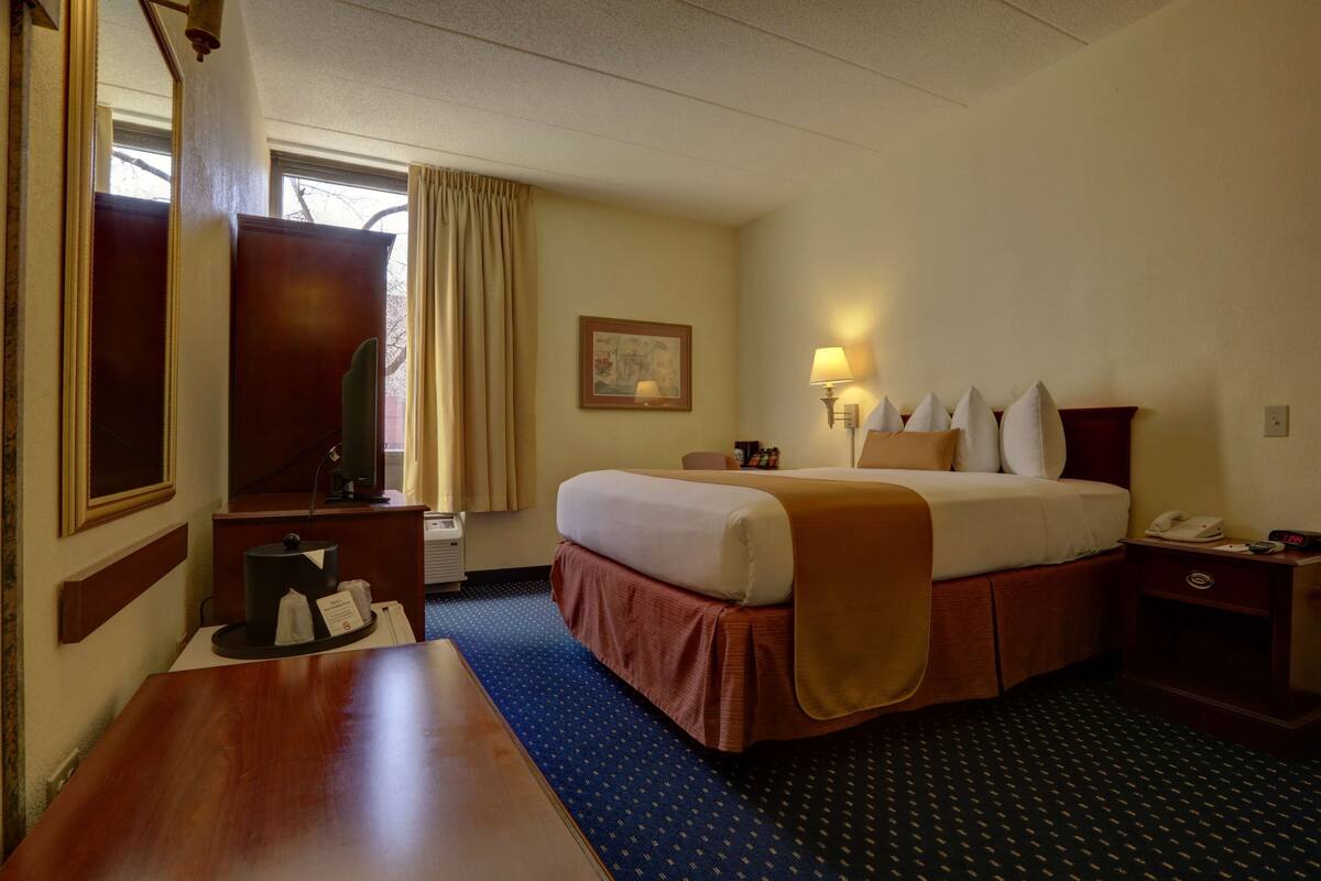 Een hotelkamer met een bed, nachtkastje, lamp en een raam met gordijnen.