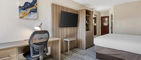 Una camera d'albergo con un letto, una scrivania, una sedia, televisione, armadio e pavimento rivestito di moquette.