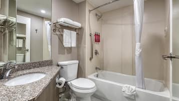 Un baño con lavamanos de granito, inodoro, bañera y cortina de ducha.