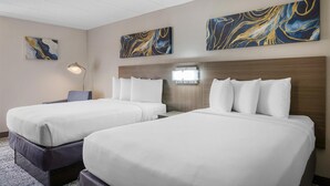 Habitación de hotel con dos camas, una mesita de noche, una lámpara y arte abstracto en las paredes.