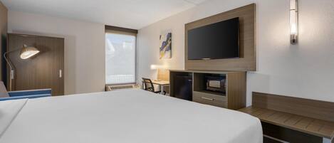 A hotel room with a large bed, a desk, a flat-screen TV, a desk lamp, and a wall-mounted TV.