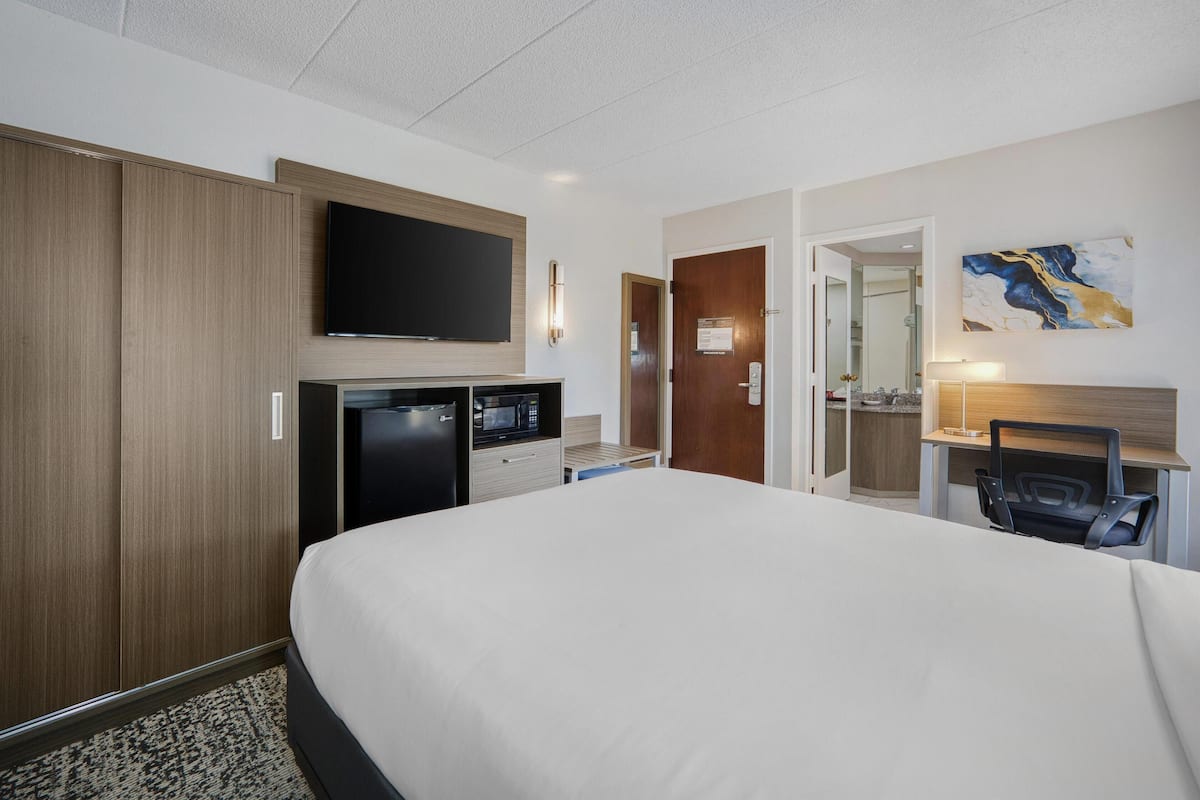 Een hotelkamer met een groot bed, een aan de muur bevestigde televisie, een bureau met stoel, en een magnetron.