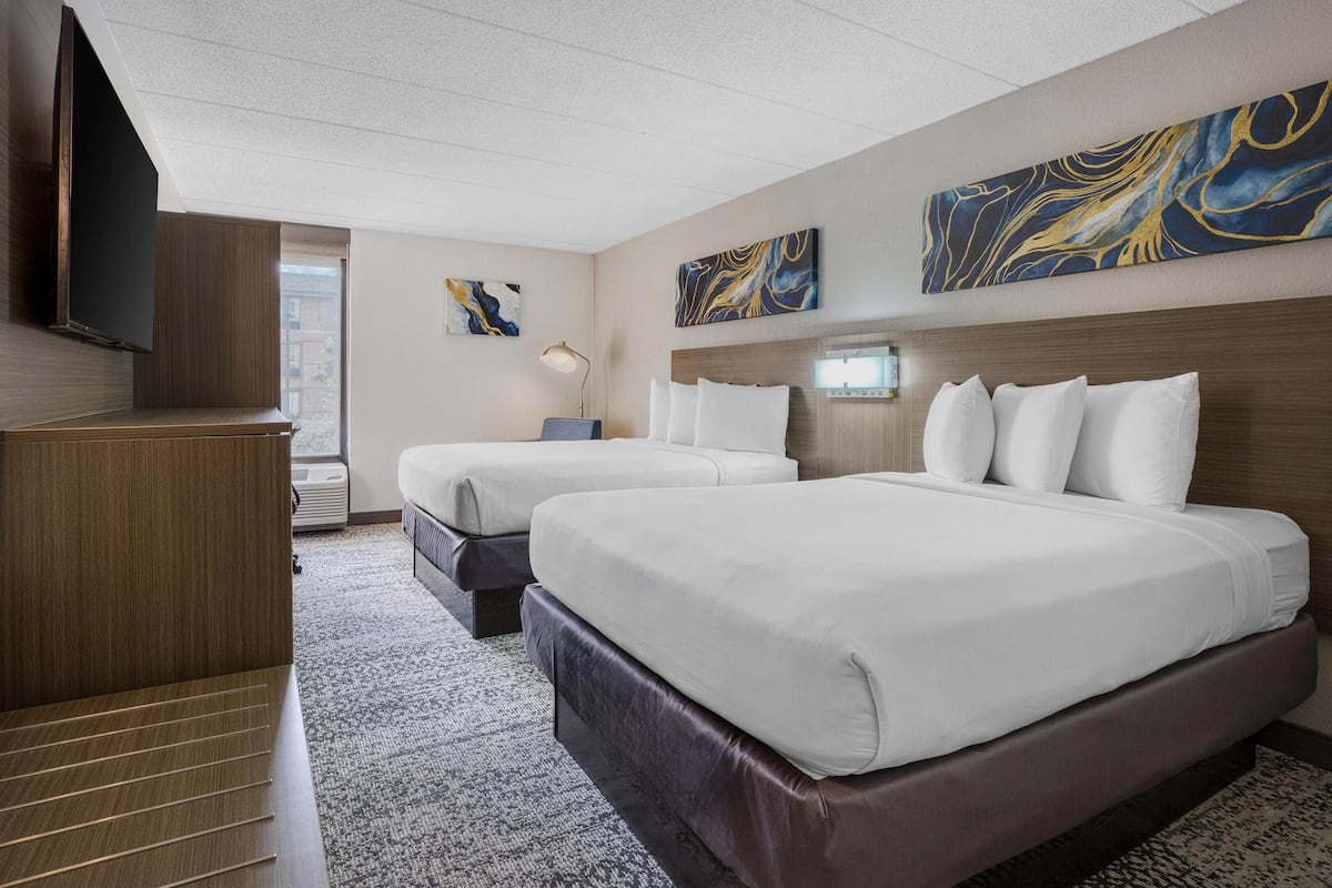 Een hotelkamer met twee bedden, een televisie, kunstwerken aan de muur en een raam.