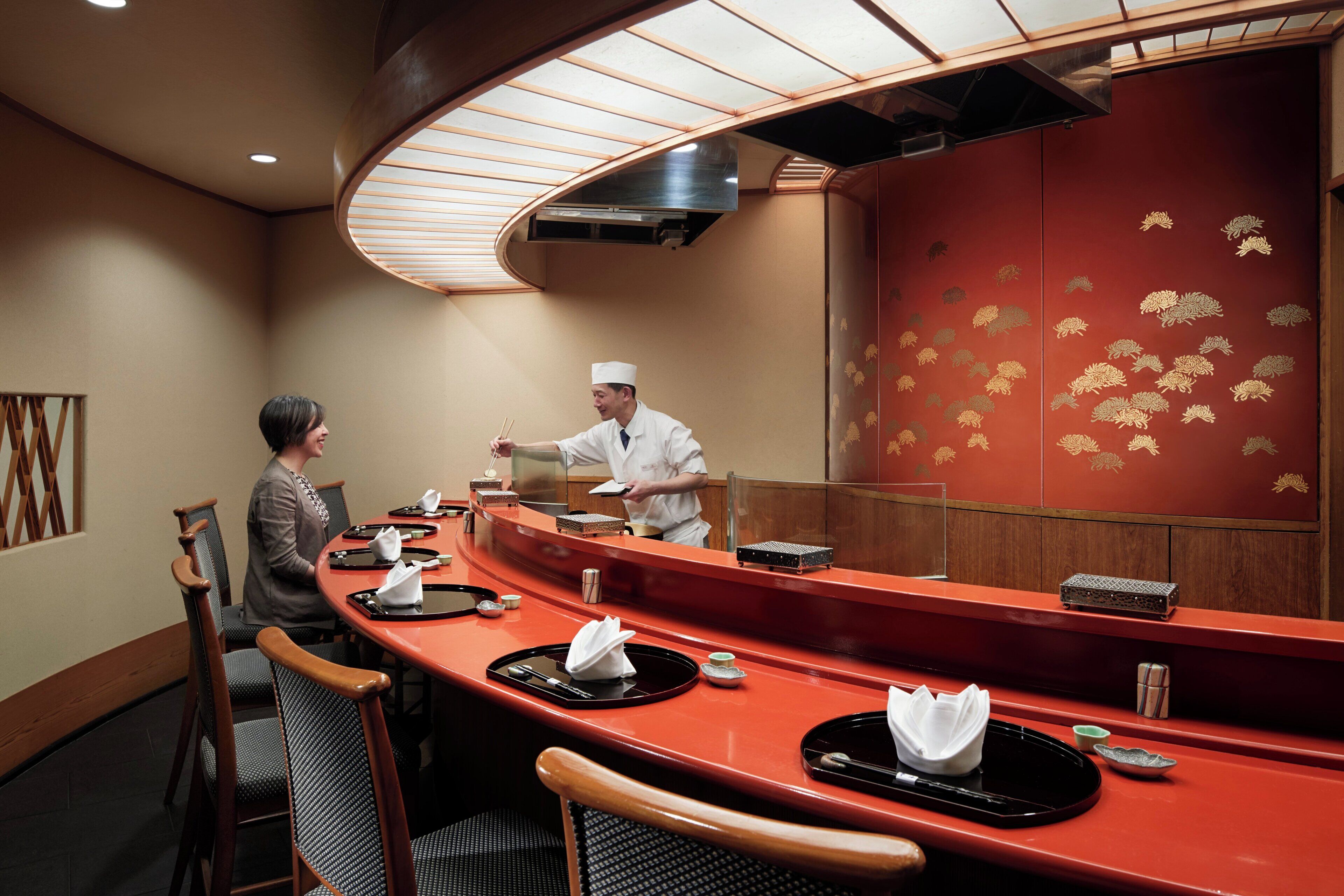 A restaurant with a curved counter, wooden chairs, and a red wall with gold patterns.