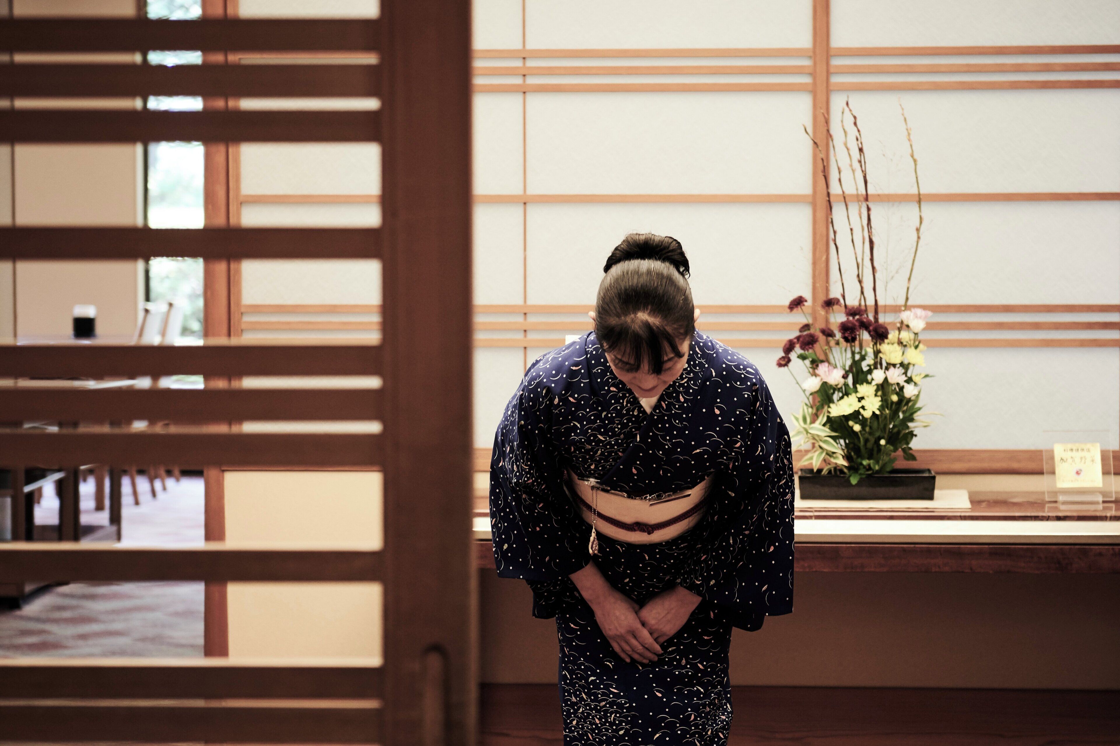 Un interior japonés tradicional con suelo de tatami, puerta corrediza de madera y un arreglo floral.