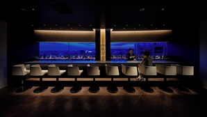 A bar area with a city view, bar stools, and a bartender.