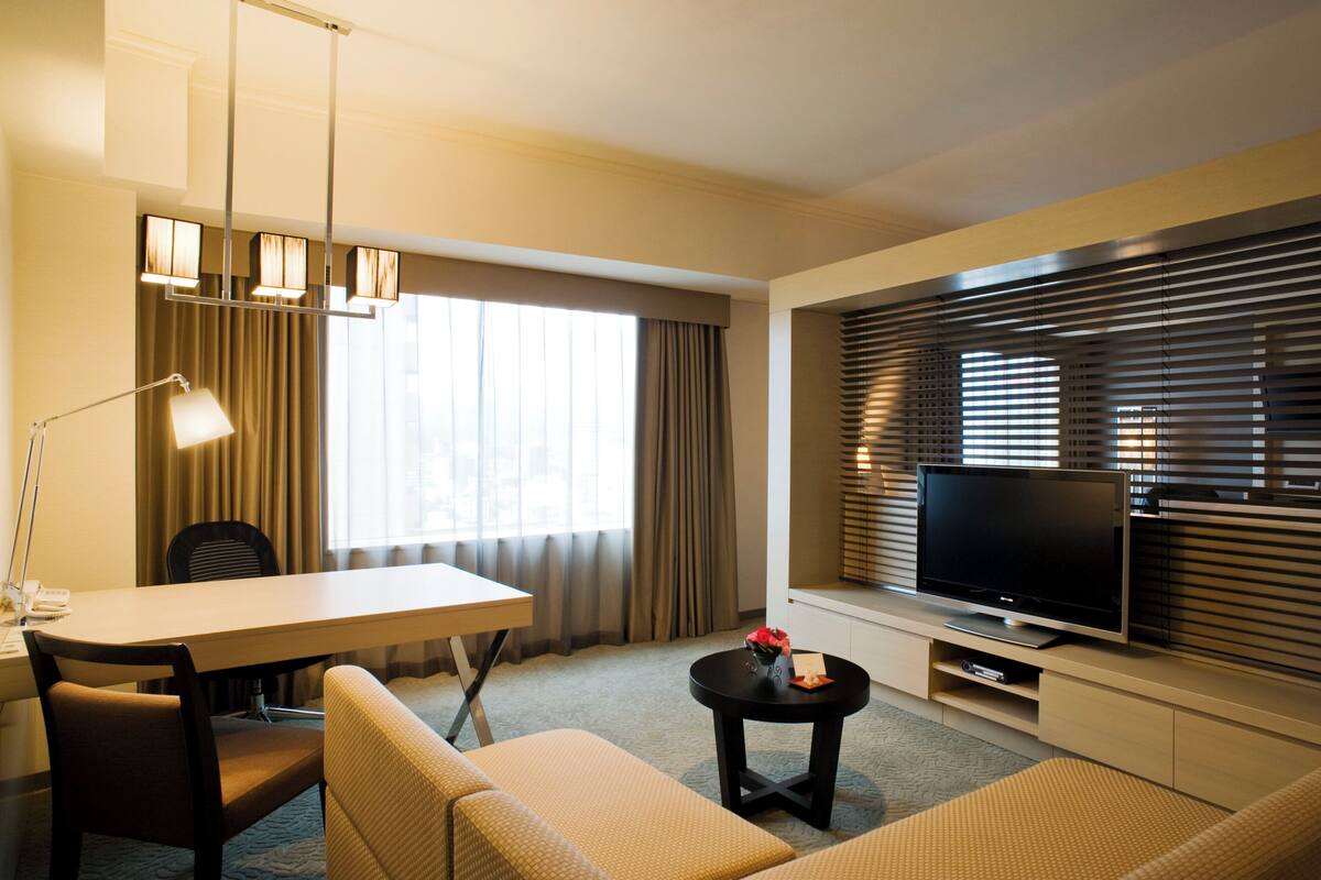 Une chambre d’hôtel équipée d’une table à manger, d’un canapé, d’une télévision et de rideaux.