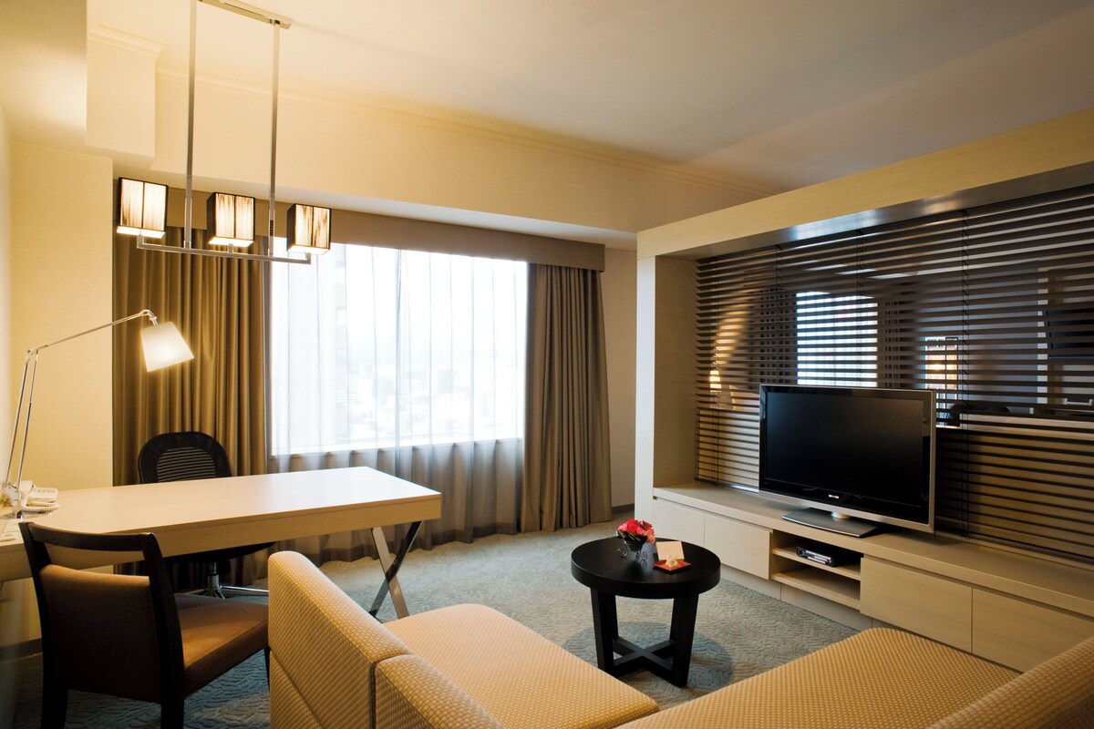 Une chambre d’hôtel équipée d’une table à manger, d’un canapé, d’une télévision et de rideaux.