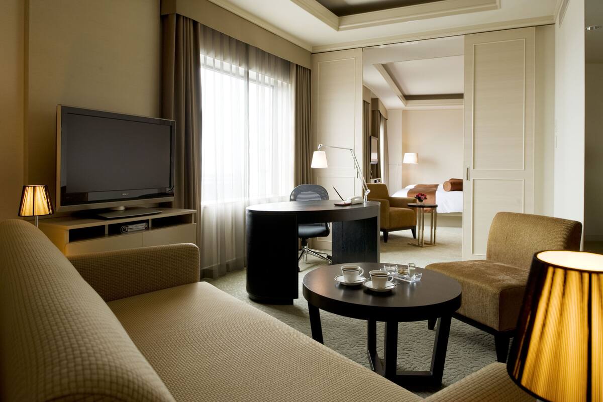 Une chambre d’hôtel équipée d’une télévision, d’un canapé, d’un fauteuil et d’une petite table avec des tasses.