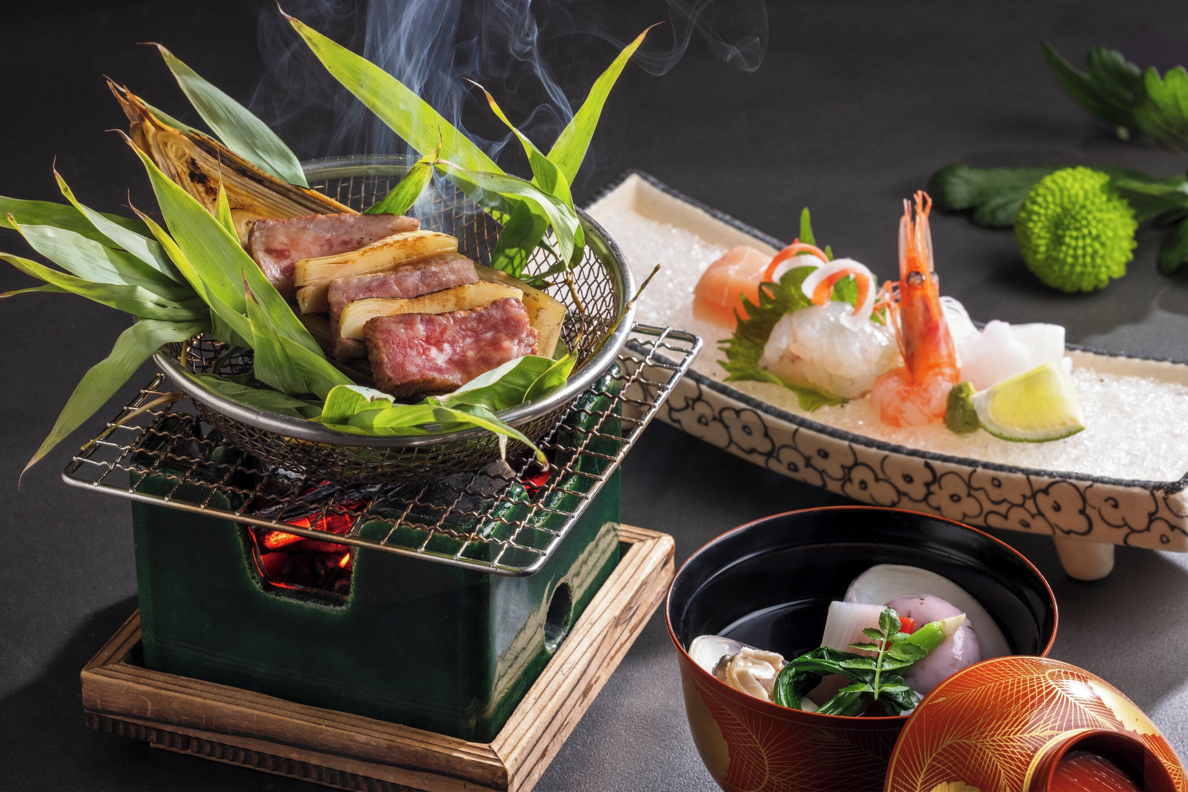 Una parrilla con comida, un bol de sashimi y una taza de té.