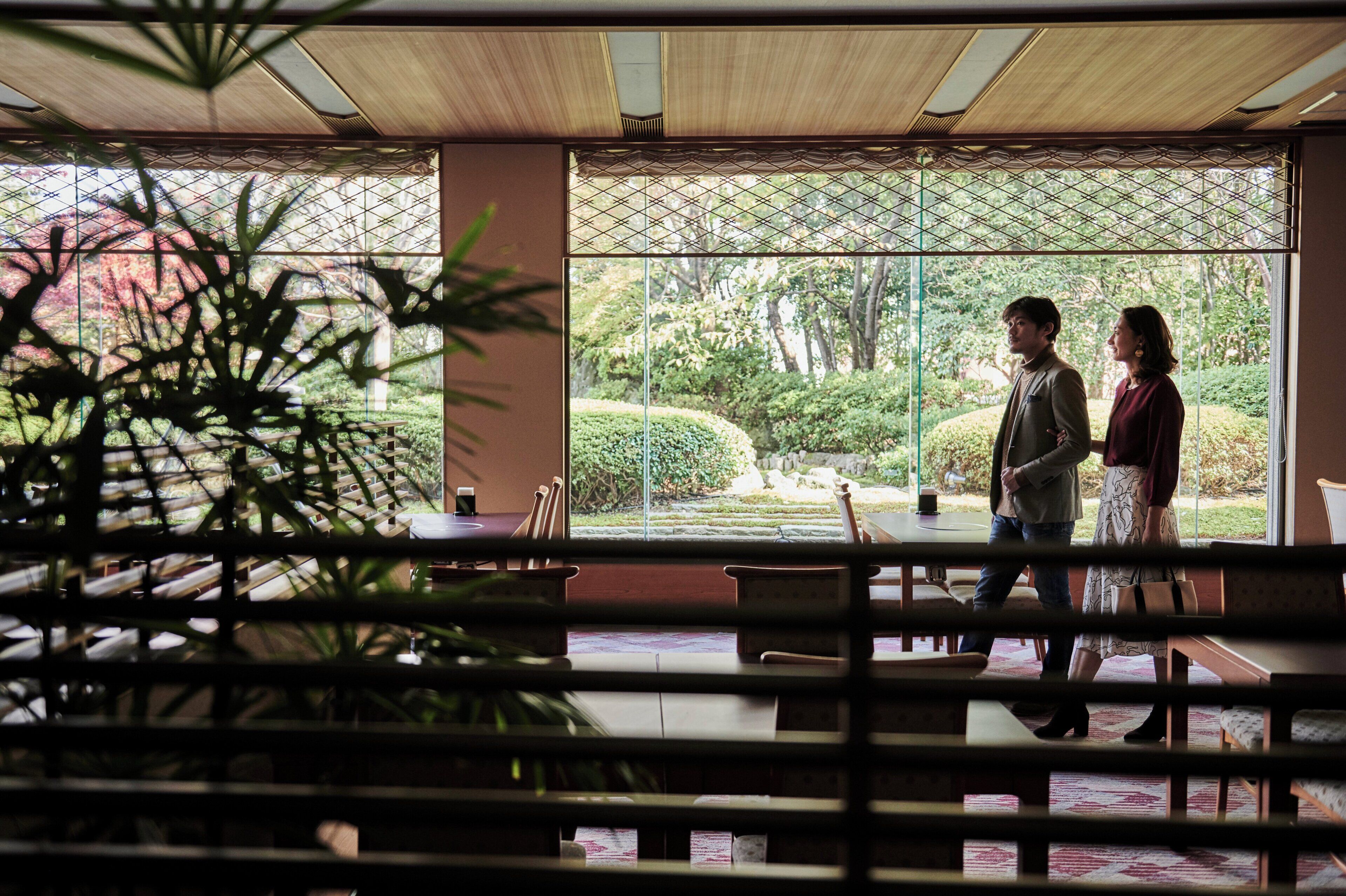 A room with large windows, wooden furniture, and a view of a garden.