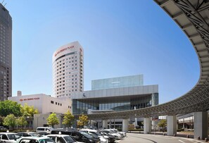 A parking lot with several cars, a building labeled 'ANA CROWNE PLAZA,' and a modern architectural structure with a curved roof.