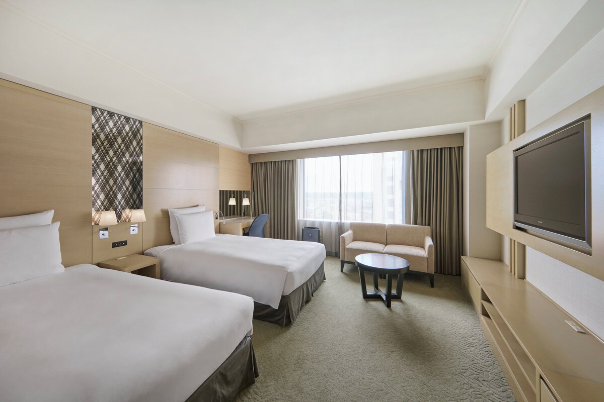 Une chambre d’hôtel avec deux lits, un canapé, une télévision et un bureau avec des lampes.