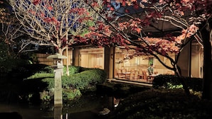 A traditional Japanese garden with a pond, stone lantern, and wooden structures.