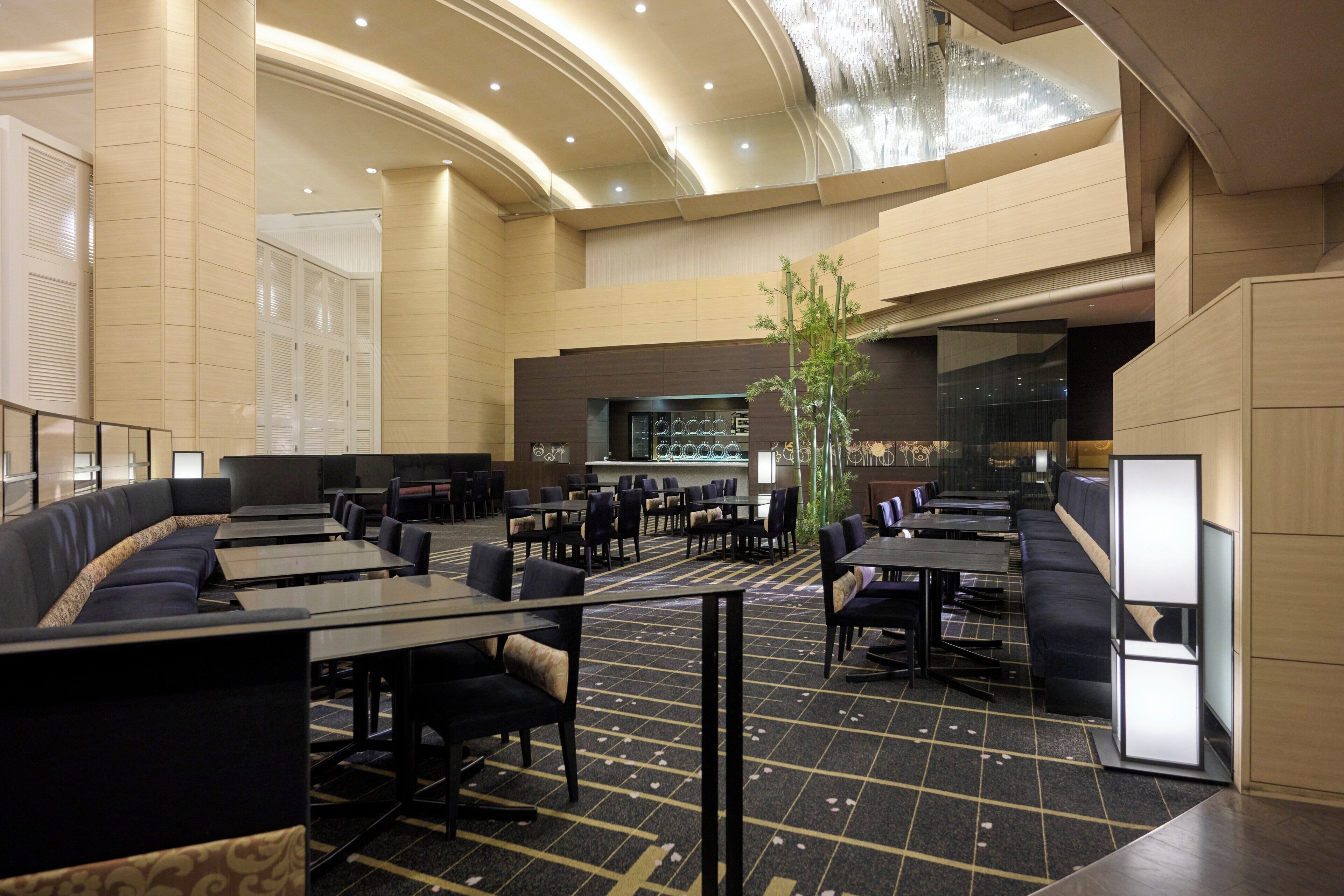 A spacious hotel lobby with a curved ceiling, seating areas, and a central plant.
