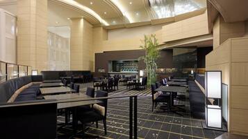 A spacious hotel lobby with a curved ceiling, seating areas, and a central plant.