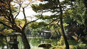 A traditional Japanese-style building by a lake with a stone lantern and neatly trimmed bushes.