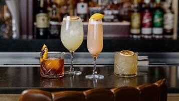 A bar with four different cocktails on a counter, with a blurred background of various bottles.
