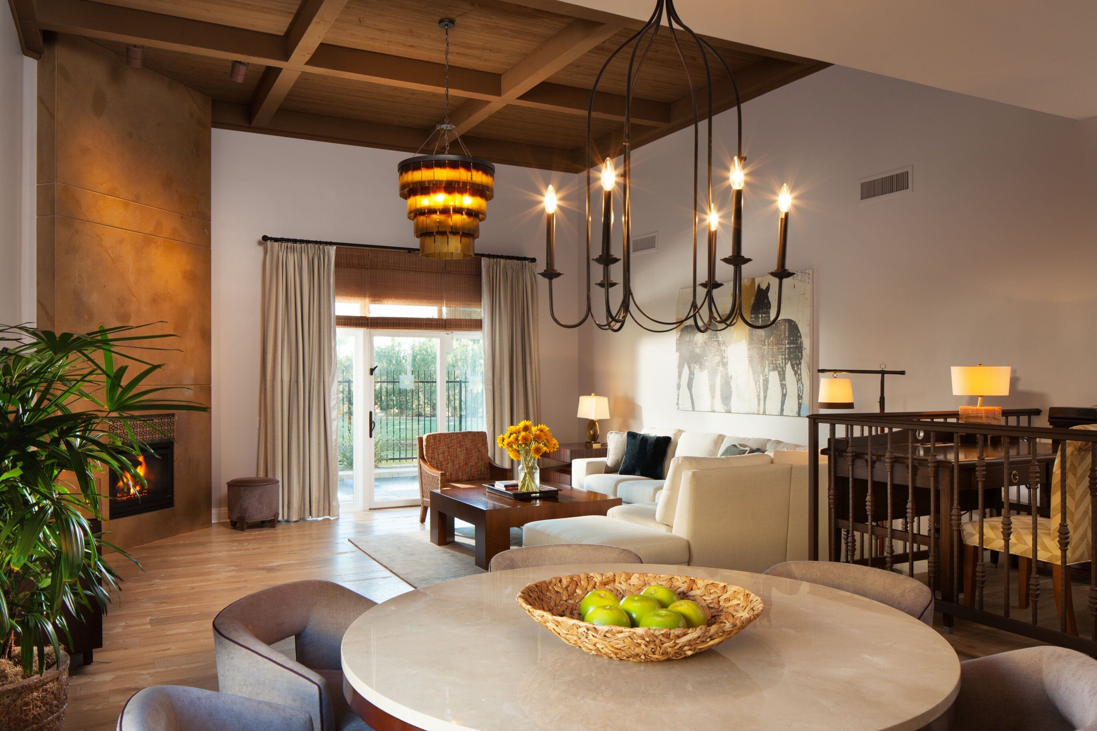 A spacious living room with a fireplace, a round table with a fruit bowl, a sofa, and a dining area with chairs.