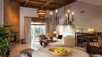 A spacious living room with a fireplace, a round table with a fruit bowl, a sofa, and a dining area with chairs.