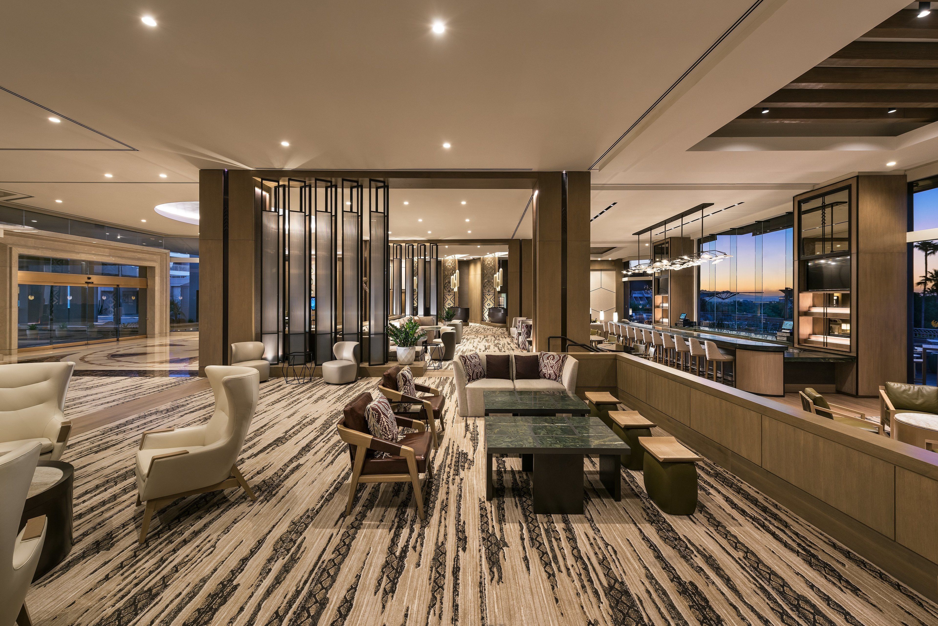 Un hall d’hôtel moderne doté d’un espace salon, d’un bar et d’une grande fenêtre donnant sur la ville.