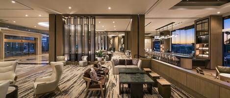 Un hall d’hôtel moderne doté d’un espace salon, d’un bar et d’une grande fenêtre donnant sur la ville.