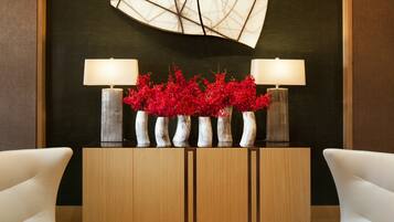 A modern lobby with two white armchairs, a wooden console table with lamps and red flowers, and a large abstract wall piece.